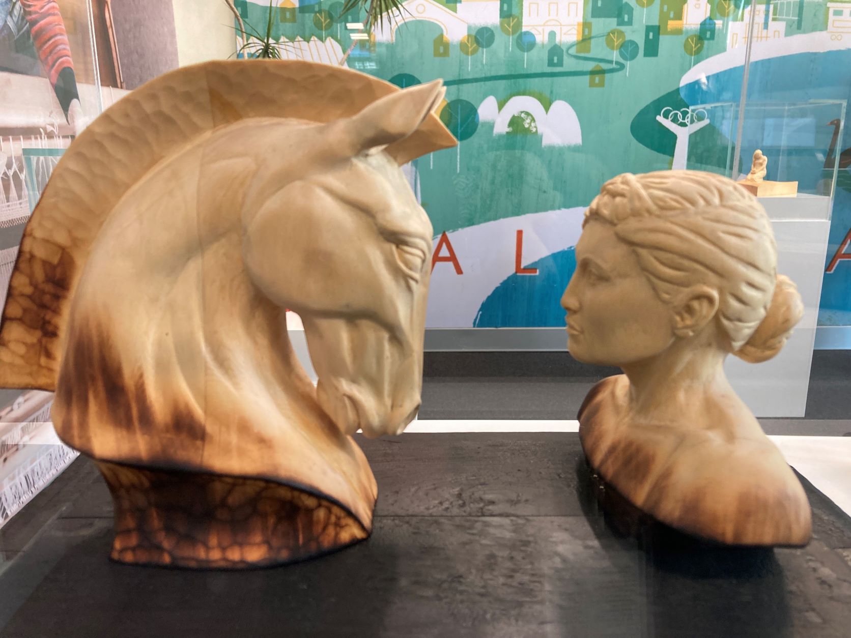 Sculpture of a horses head facing a female carved from wood.